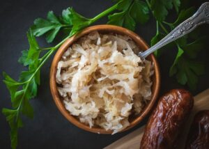 uma tigela com chucrute. ao lado de uma folha de rúcula e linguiça