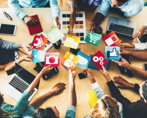 várias pessoal numa mesa com seus equipamentos tecnológicos de simbolos das redes sociais